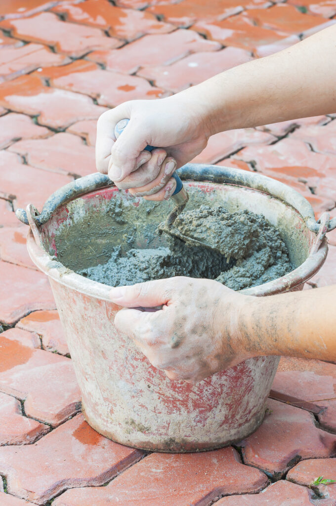 Hand holding trowel mixing mortar in a bucket